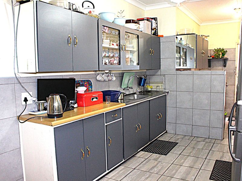 A functional kitchen featuring grey cabinetry, tiled backsplash, and tiled flooring, offering a practical layout with ample storage space.