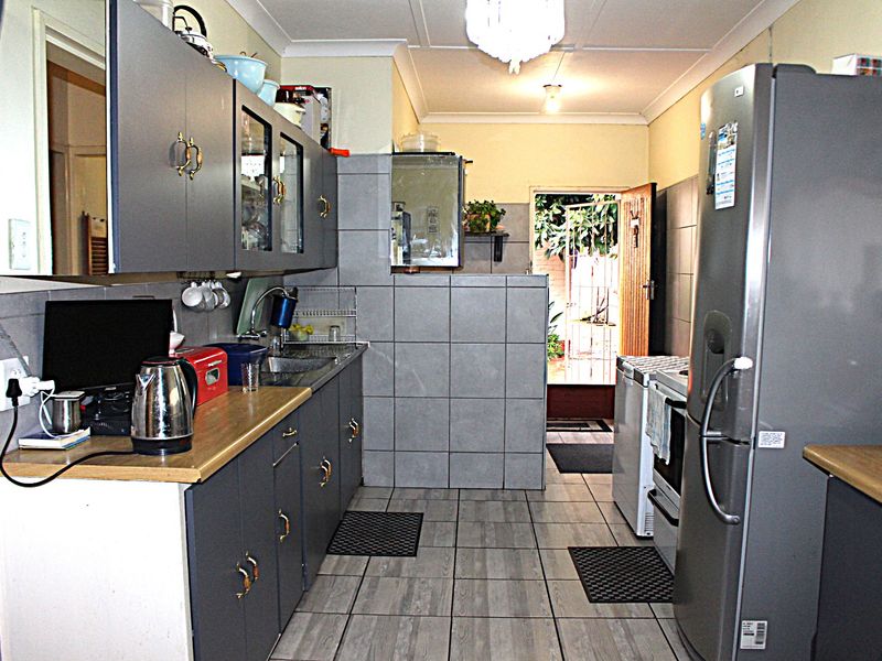 A functional galley-style kitchen featuring grey cabinetry, tiled splashbacks, and tiled flooring, with direct access to an outdoor area.