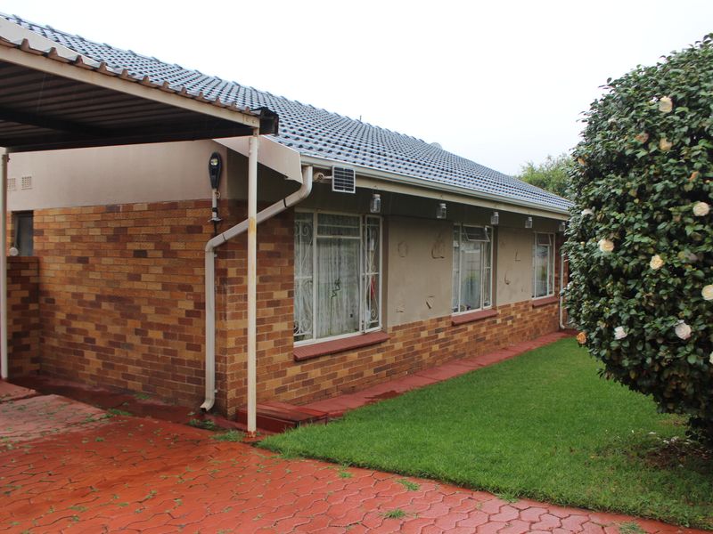 Front exterior view of a single-story brick house featuring a tiled roof, attached carport, and paved driveway area.