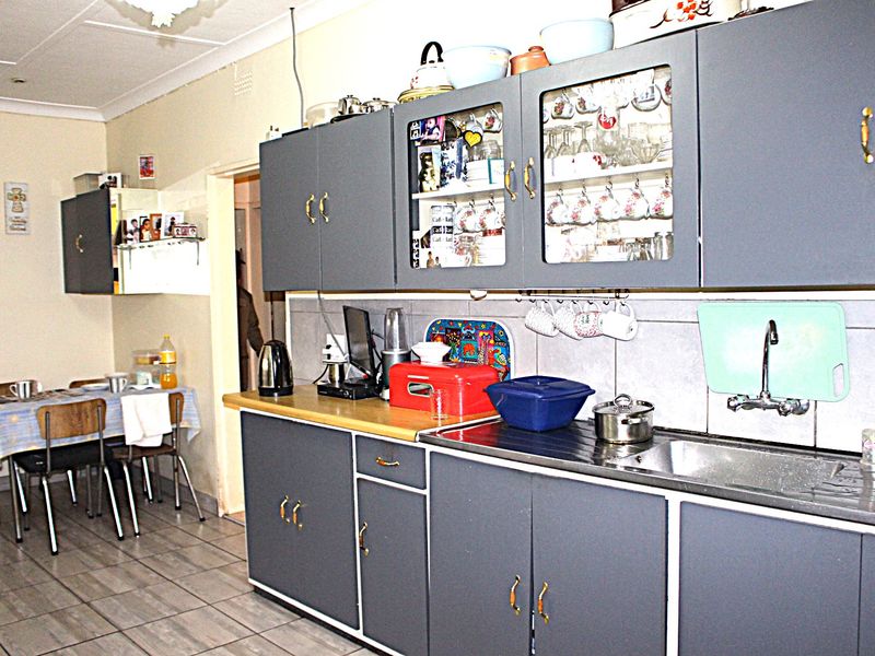 A functional kitchen featuring grey built-in cabinetry, a stainless steel sink, tiled backsplash, and tiled flooring, with an adjacent dining area.