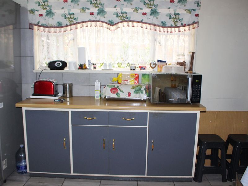 A functional kitchen area featuring grey cabinetry, a laminate countertop, and a tiled backsplash under a window.