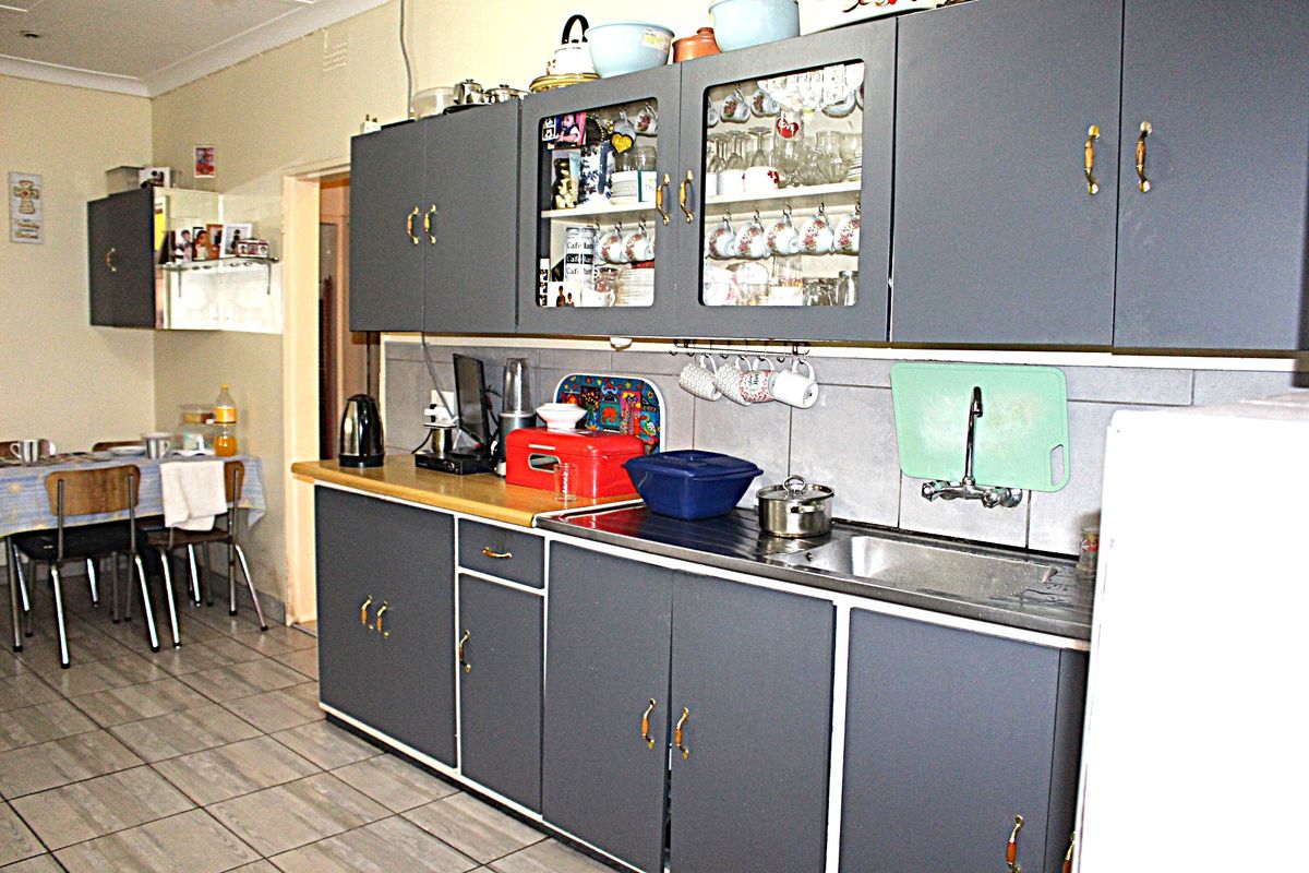 A functional kitchen featuring grey cabinetry, tiled splashbacks, and a stainless steel sink, offering a practical layout with potential for modern updates.