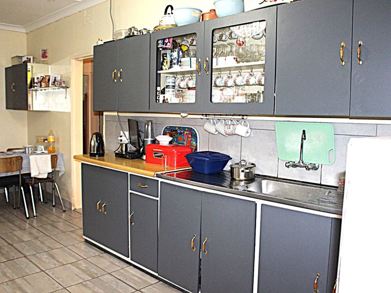 A functional kitchen featuring grey cabinetry, tiled splashbacks, and a stainless steel sink, offering a practical layout with potential for modern updates.