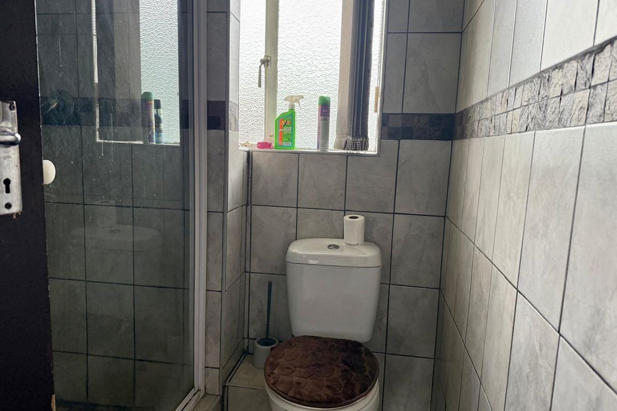 A functional bathroom featuring a shower enclosure, toilet, and tiled wall finishes with an obscured glass window for natural light.