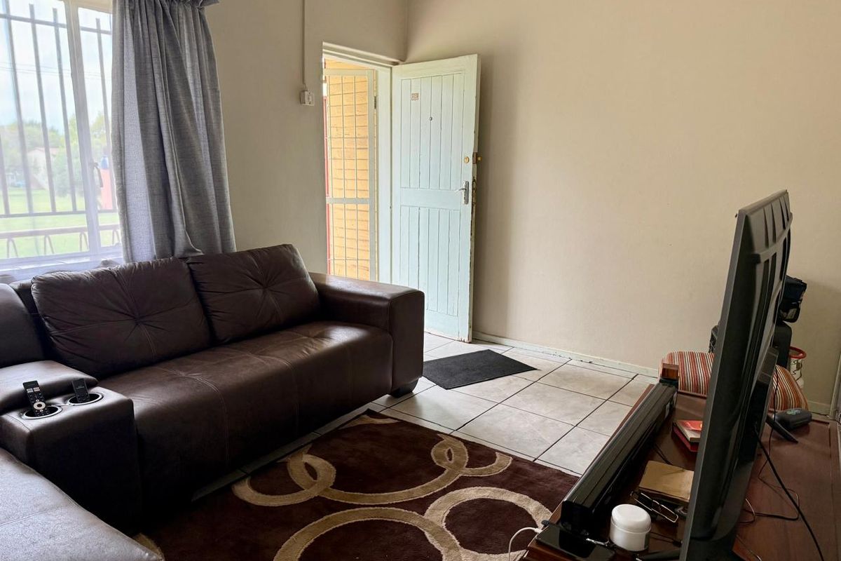 A functional living room featuring tiled flooring, natural light through a window with security bars, and direct access to the exterior via a security gate.