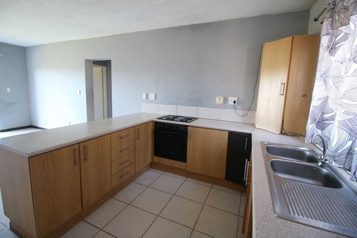 A functional kitchen featuring light wood cabinetry, laminate countertops, a built-in oven and hob, and tiled flooring, ready for a modern update.