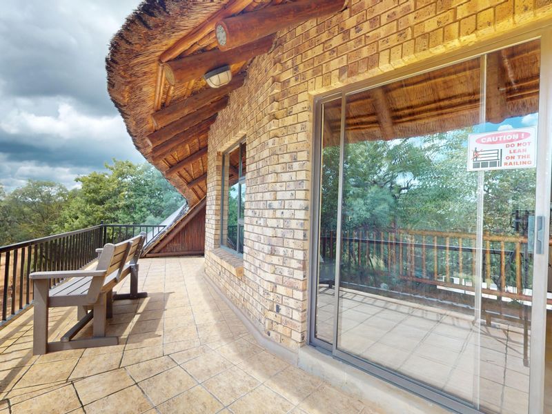 A covered balcony featuring a traditional thatched roof, exposed timber beams, face brick exterior, and a metal balustrade overlooking the surrounding landscape.