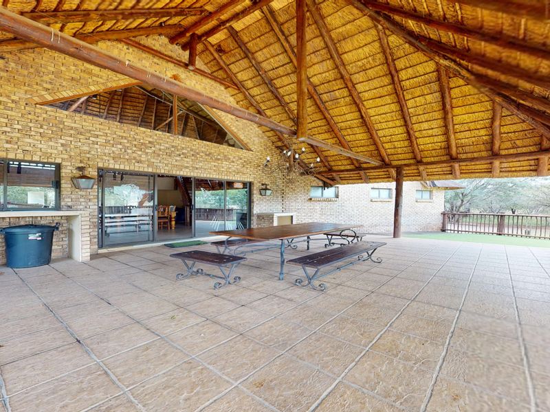 Spacious covered patio featuring a traditional thatched roof, exposed timber beams, face brick walls, and tiled flooring, ideal for outdoor entertaining.