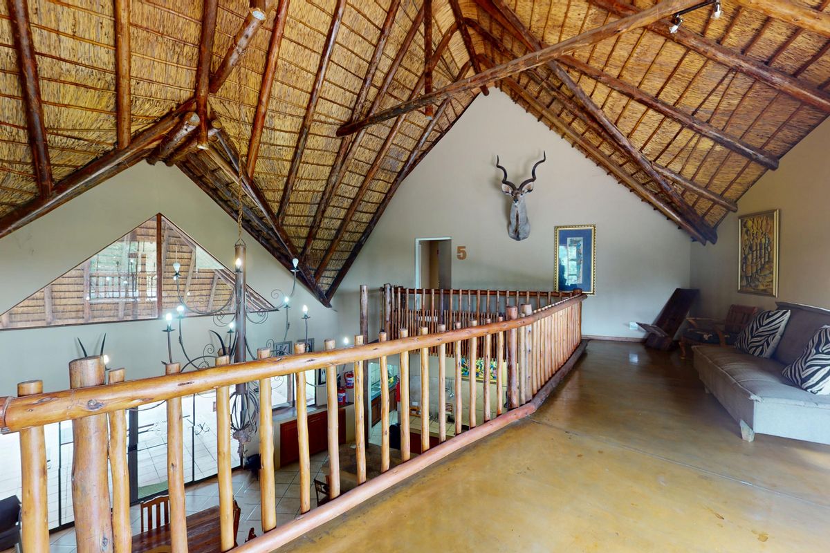 A spacious mezzanine living area featuring a high vaulted thatched roof with exposed timber trusses and a rustic timber balustrade overlooking the lower level.