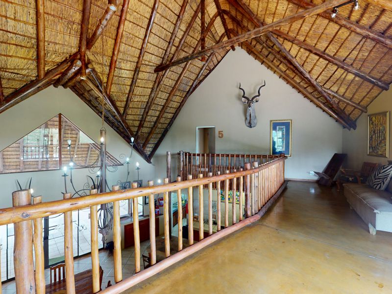 A spacious mezzanine living area featuring a high vaulted thatched roof with exposed timber trusses and a rustic timber balustrade overlooking the lower level.