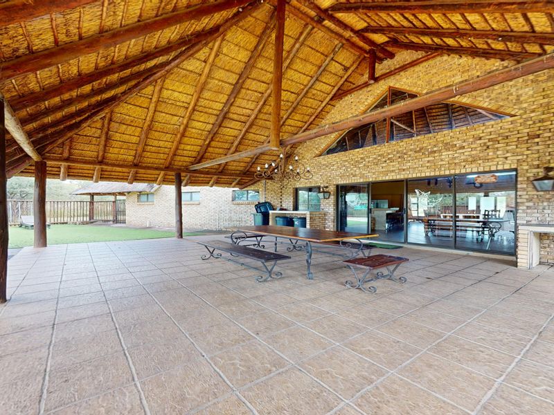 Spacious covered patio featuring a traditional thatched roof, exposed timber beams, brick walls, and a built-in braai area, perfect for outdoor entertaining.