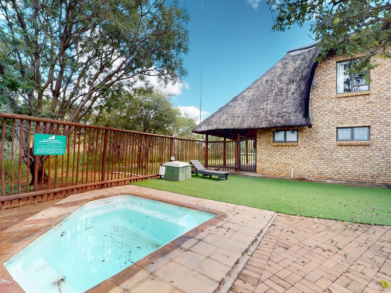 Outdoor pool area featuring a small plunge pool, paved surround, artificial lawn, and a two-story brick building with a traditional thatched roof.