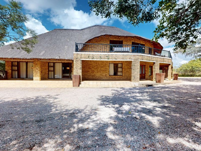 A spacious double-story house featuring a traditional thatch roof, face brick exterior, and a wide covered patio with an upper-level balcony.