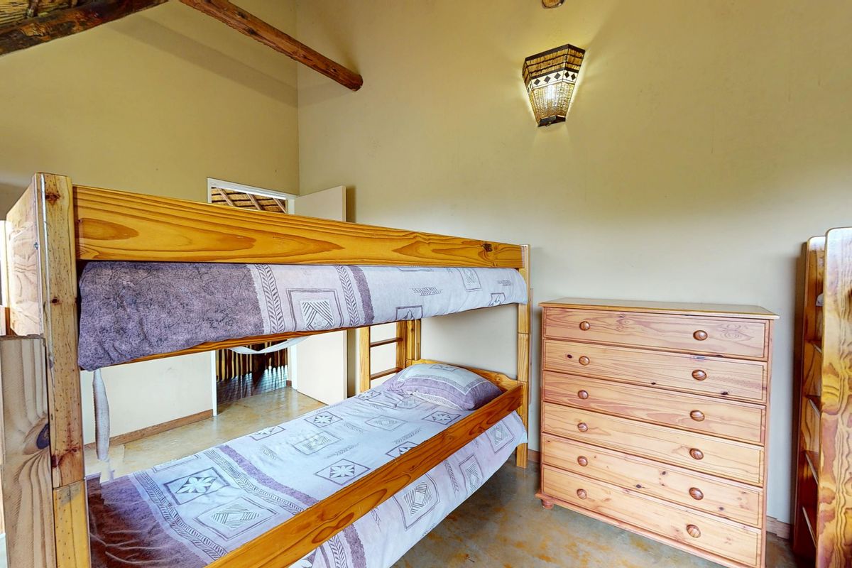 A bedroom featuring a high vaulted ceiling with exposed timber rafters, thatched roofing, and tiled flooring.