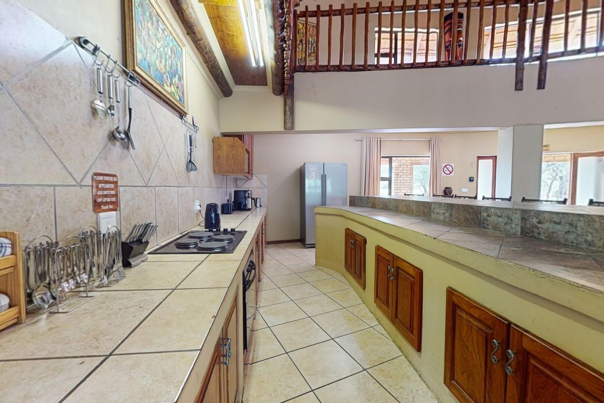 Spacious kitchen featuring tiled countertops, built-in hob and oven, wooden cabinetry, and an open-plan layout overlooking a mezzanine level.