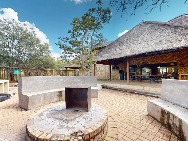 Outdoor entertainment area featuring a thatched roof patio, brick paving, and a central built-in fire pit with concrete seating.