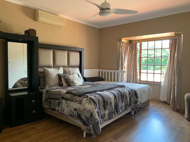Spacious bedroom featuring laminate flooring, a ceiling fan, split-system air conditioning, and a large bay window providing natural light.