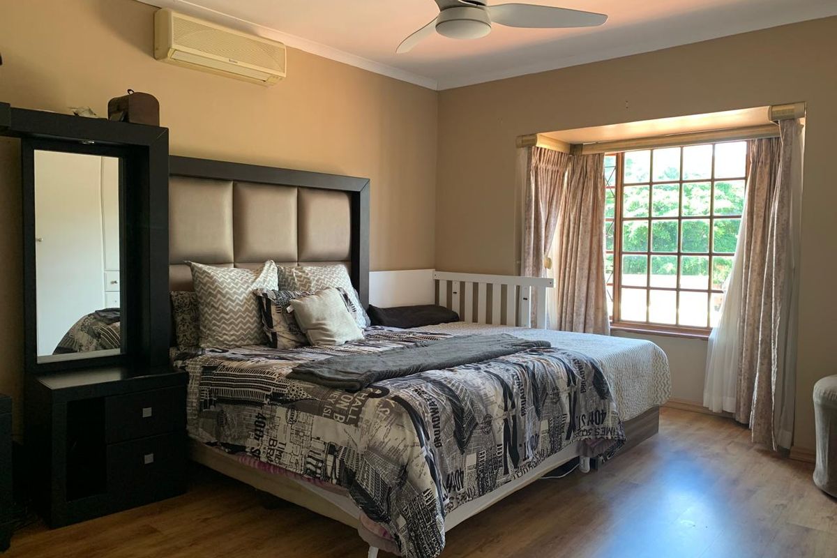 Spacious bedroom featuring laminate flooring, a ceiling fan, split-system air conditioning, and a large bay window providing natural light.
