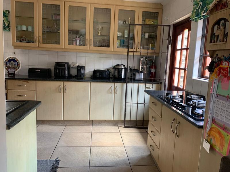 A functional kitchen featuring light wood cabinetry, granite countertops, a gas hob, and tiled flooring, offering a practical layout for daily meal preparation.