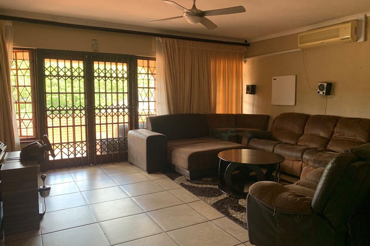 A living room featuring tiled flooring, a ceiling fan, a wall-mounted air conditioner, and a security gate leading to the exterior.
