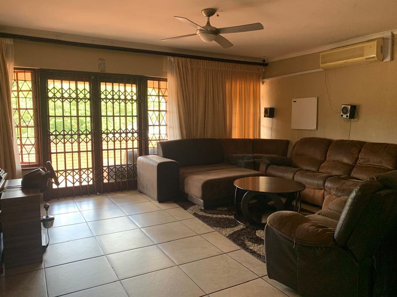 A living room featuring tiled flooring, a ceiling fan, a wall-mounted air conditioner, and a security gate leading to the exterior.