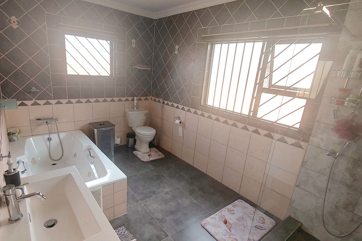 A spacious bathroom featuring a built-in bathtub, separate shower enclosure, toilet, and a modern vanity basin with tiled finishes throughout.