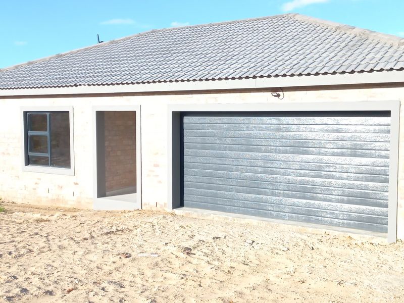 A detached garage featuring a modern roller door, tiled roof, and face brick exterior, currently set within an unfinished landscape.