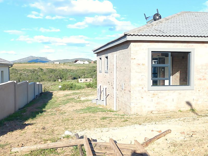 Rear view of a residential property featuring exposed brickwork, aluminium window frames, a solar water heater, and an unfinished garden area.