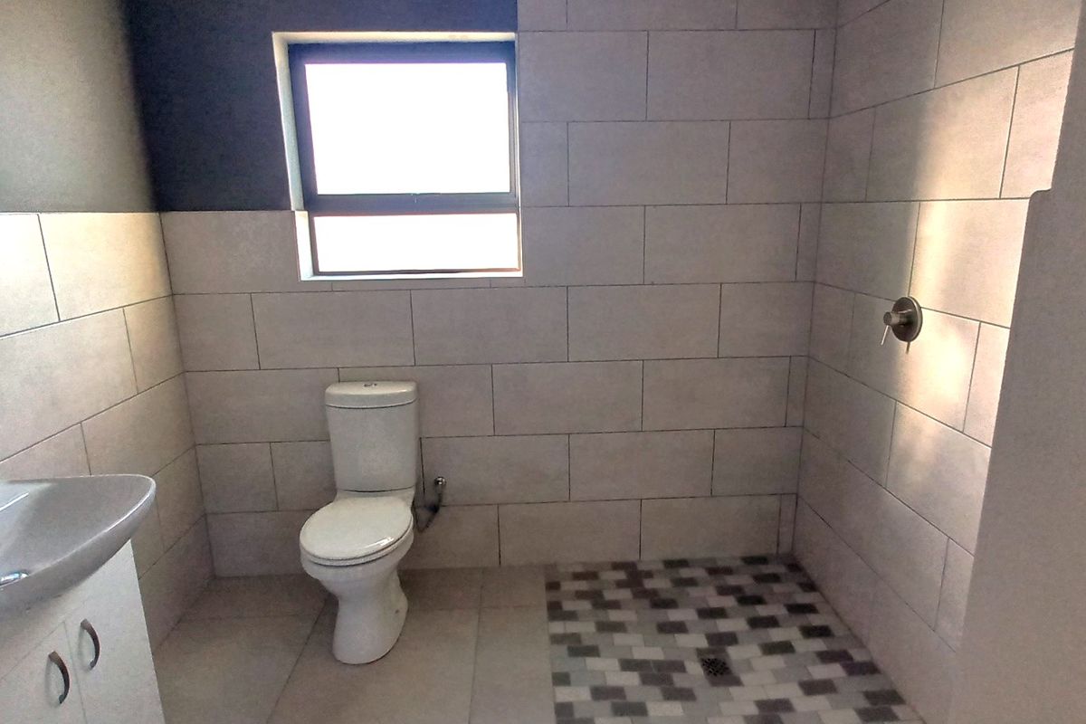 A modern, clean bathroom featuring a walk-in shower, wall-mounted vanity with basin, and a toilet, finished with neutral wall and floor tiling.