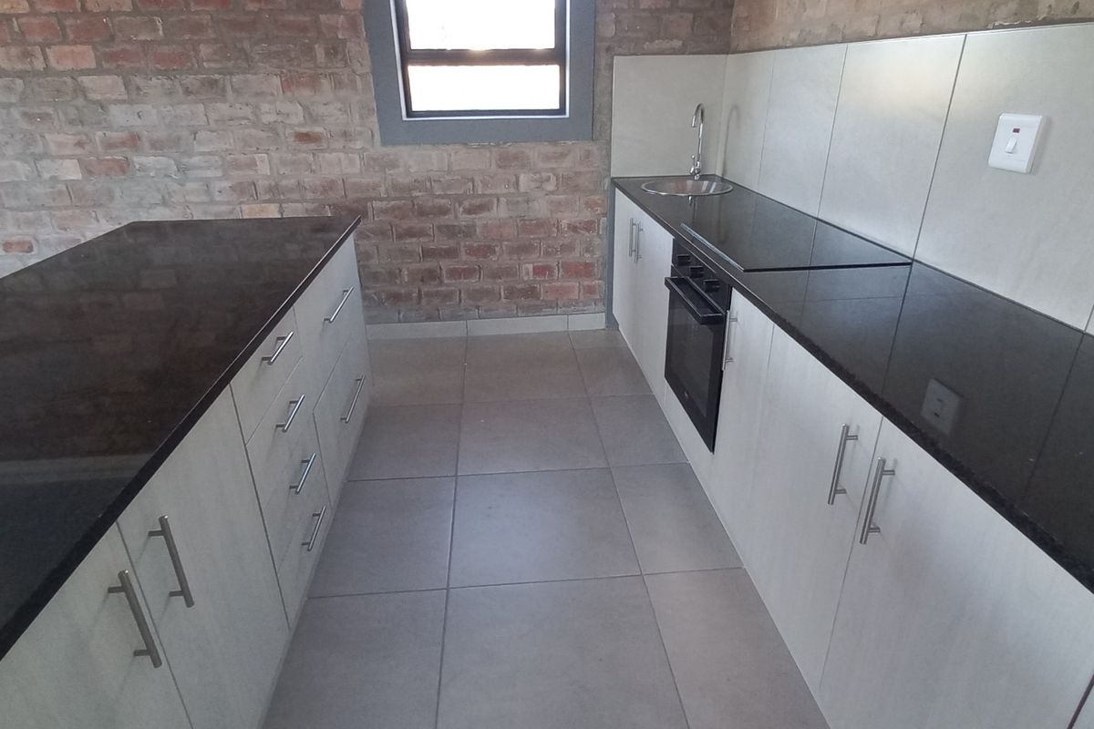 Modern kitchen featuring exposed brick walls, granite countertops, built-in cabinetry, and integrated oven and hob.