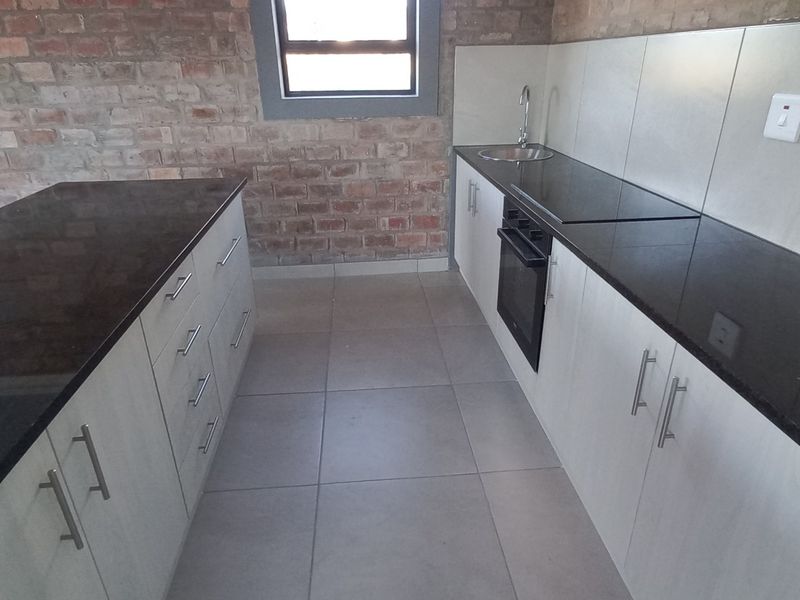 Modern kitchen featuring exposed brick walls, granite countertops, built-in cabinetry, and integrated oven and hob.
