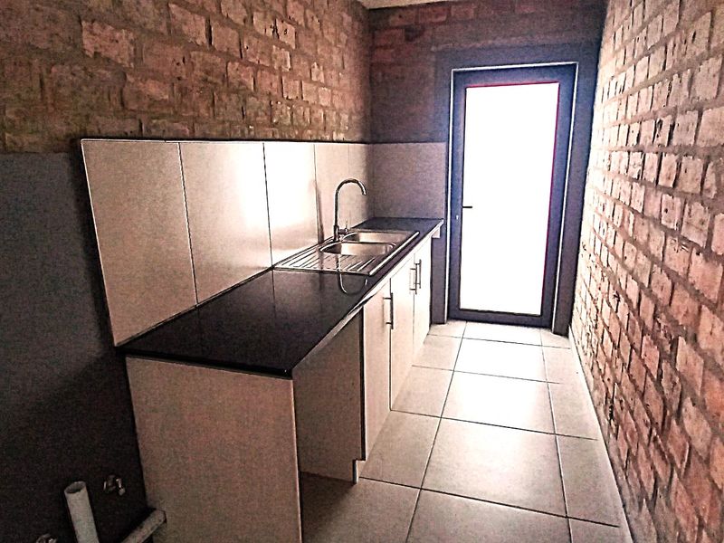 A functional scullery area featuring exposed brick walls, built-in cabinetry with a stone countertop, stainless steel sink, and direct access to the exterior.