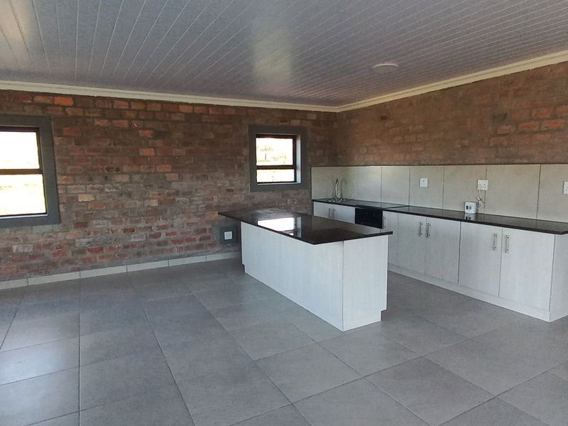 Spacious open-plan kitchen and living area featuring exposed brick walls, modern cabinetry with granite countertops, and neutral tiled flooring.