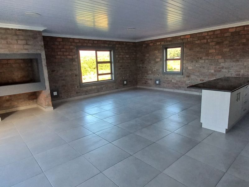 Spacious open-plan living area featuring exposed brick walls, tiled flooring, a built-in fireplace, and a modern kitchen island.