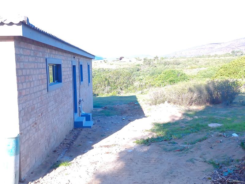Rear view of the property showing the brick exterior, garage access, and surrounding natural landscape.