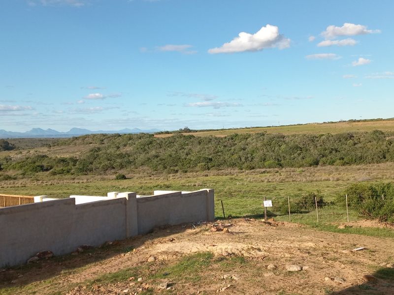 Expansive rural landscape view featuring a concrete boundary wall and timber deck, overlooking natural vegetation and distant mountain ranges.