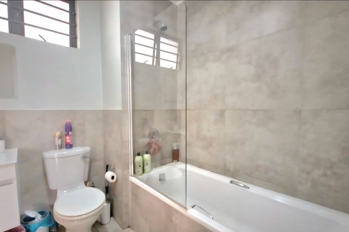 A modern bathroom featuring neutral wall tiles, a built-in bathtub with a glass shower screen, and a white vanity basin.