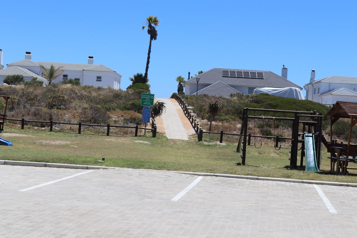 A view of the rear exterior area featuring a paved walkway leading between residential properties, with solar panels visible on the roof and a parking area.
