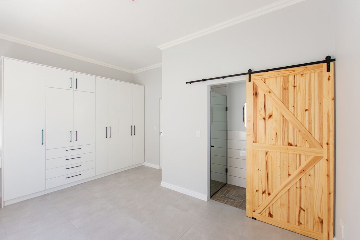 Spacious bedroom featuring extensive built-in white cabinetry, modern tiled flooring, and a rustic timber sliding barn door leading to an en-suite bathroom.