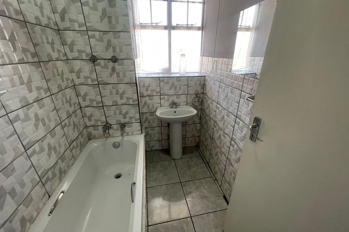 A compact bathroom featuring a standard bathtub, pedestal basin, and tiled finishes throughout, offering a functional space ready for modernization.