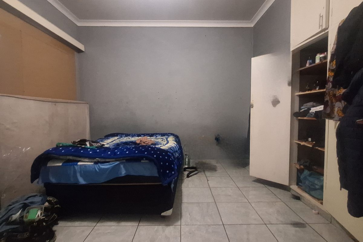 A bedroom featuring tiled flooring, built-in cupboards, and coved ceilings, currently requiring cosmetic updates and repairs to the wall finishes and cabinetry.