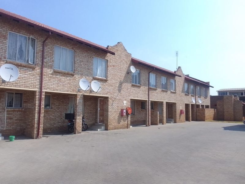 A view of the front facade of a face brick apartment complex featuring a paved driveway and multiple unit entrances.