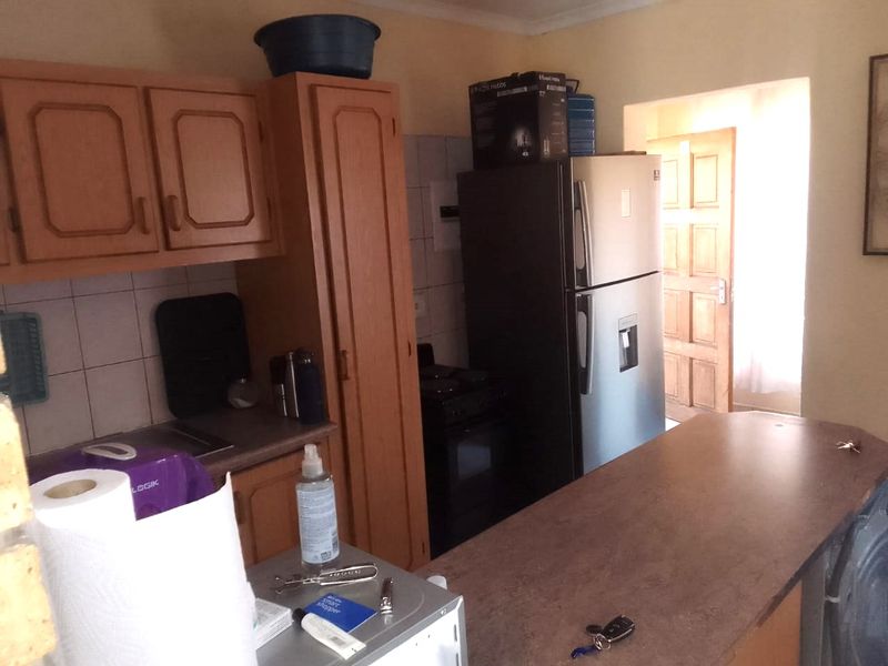 A compact kitchen featuring dated wooden cabinetry, laminate countertops, and tiled splashbacks, providing a functional layout with space for a freestanding stove.
