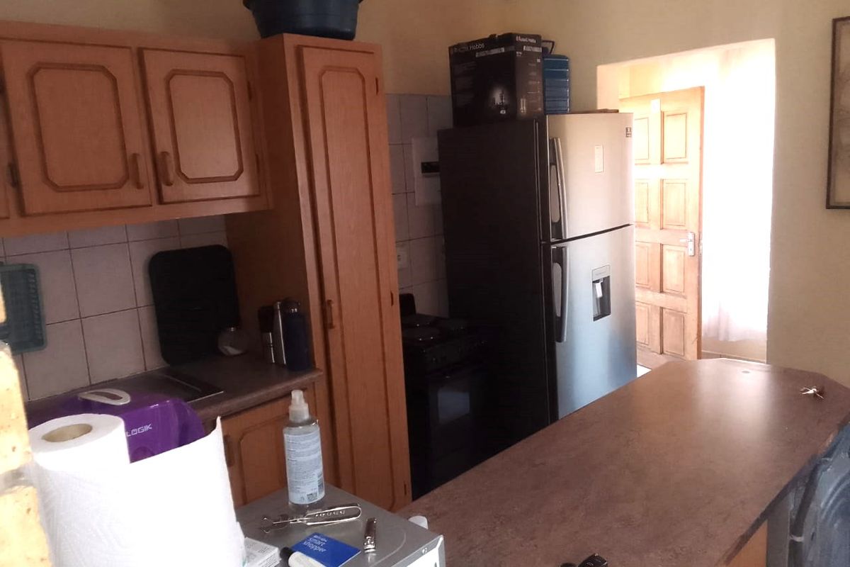 A compact kitchen featuring dated wooden cabinetry, laminate countertops, and tiled splashbacks, providing a functional layout with space for a freestanding stove.
