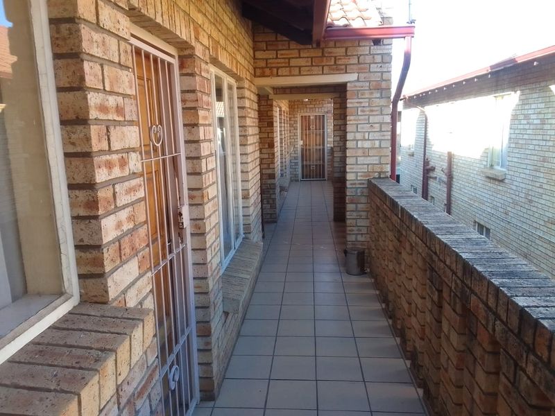 An exterior balcony walkway featuring face-brick walls, tiled flooring, and a brick balustrade, providing access to the unit entrance.