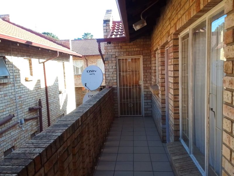 A covered balcony featuring brick walls, tiled flooring, and a secure entrance gate, providing an outdoor transition space for the flat.