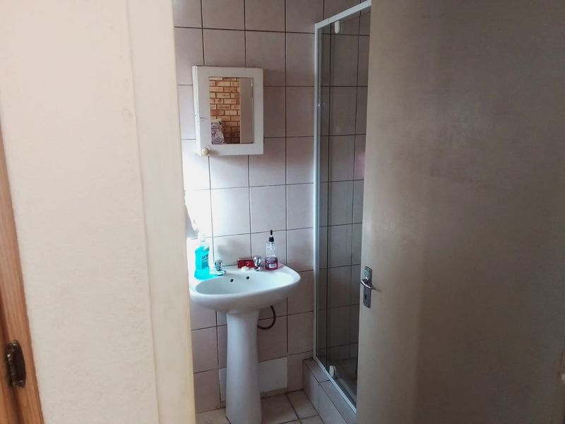 A functional bathroom featuring a pedestal basin, shower enclosure, and tiled finishes, offering a practical layout for daily use.