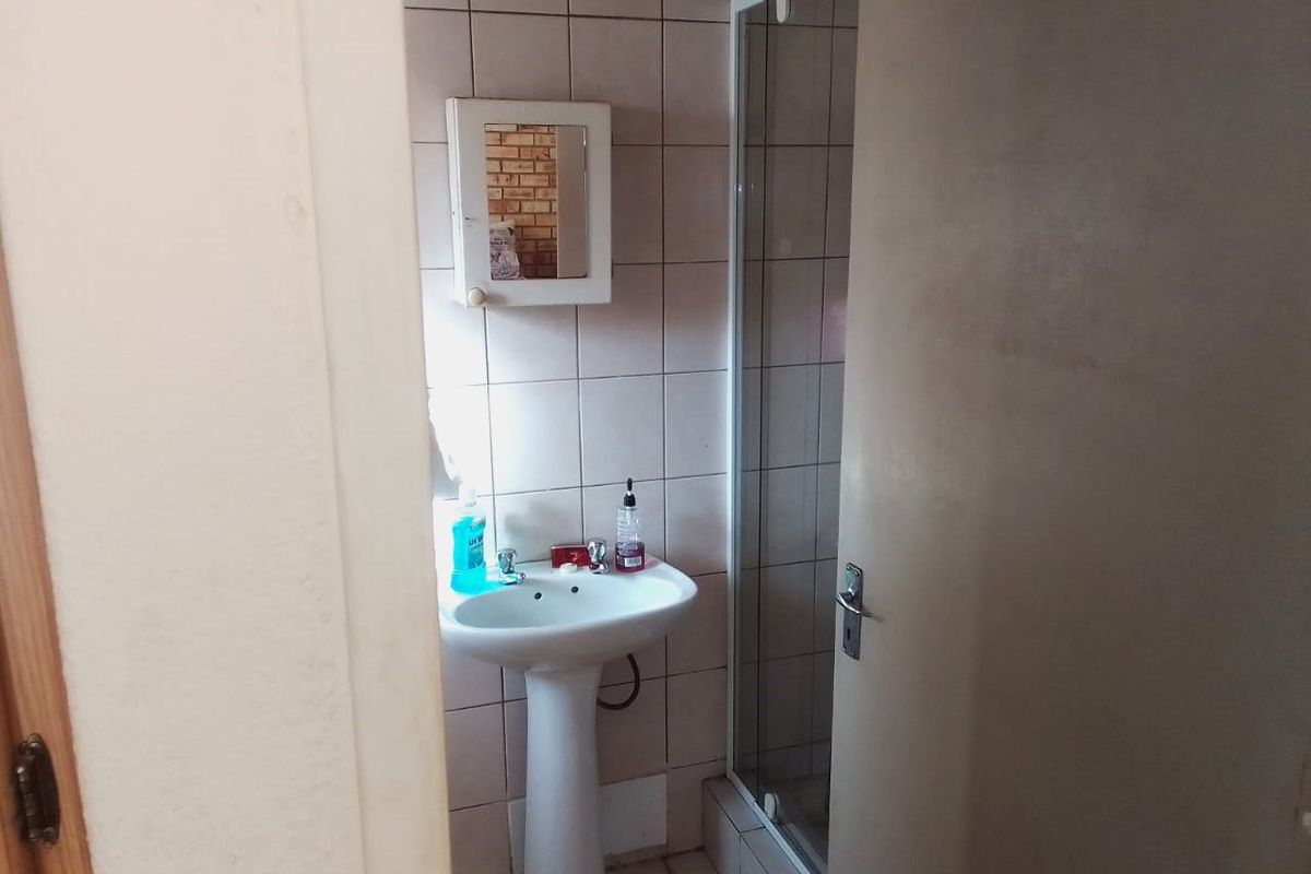 A functional bathroom featuring a pedestal basin, shower enclosure, and tiled finishes, offering a practical layout for daily use.
