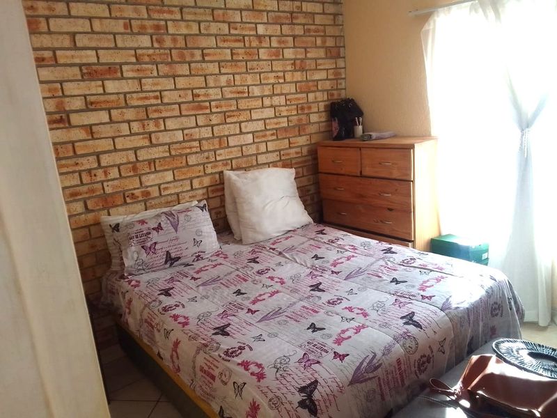 A bedroom featuring an exposed brick feature wall and tiled flooring, offering a rustic aesthetic with natural light from the window.