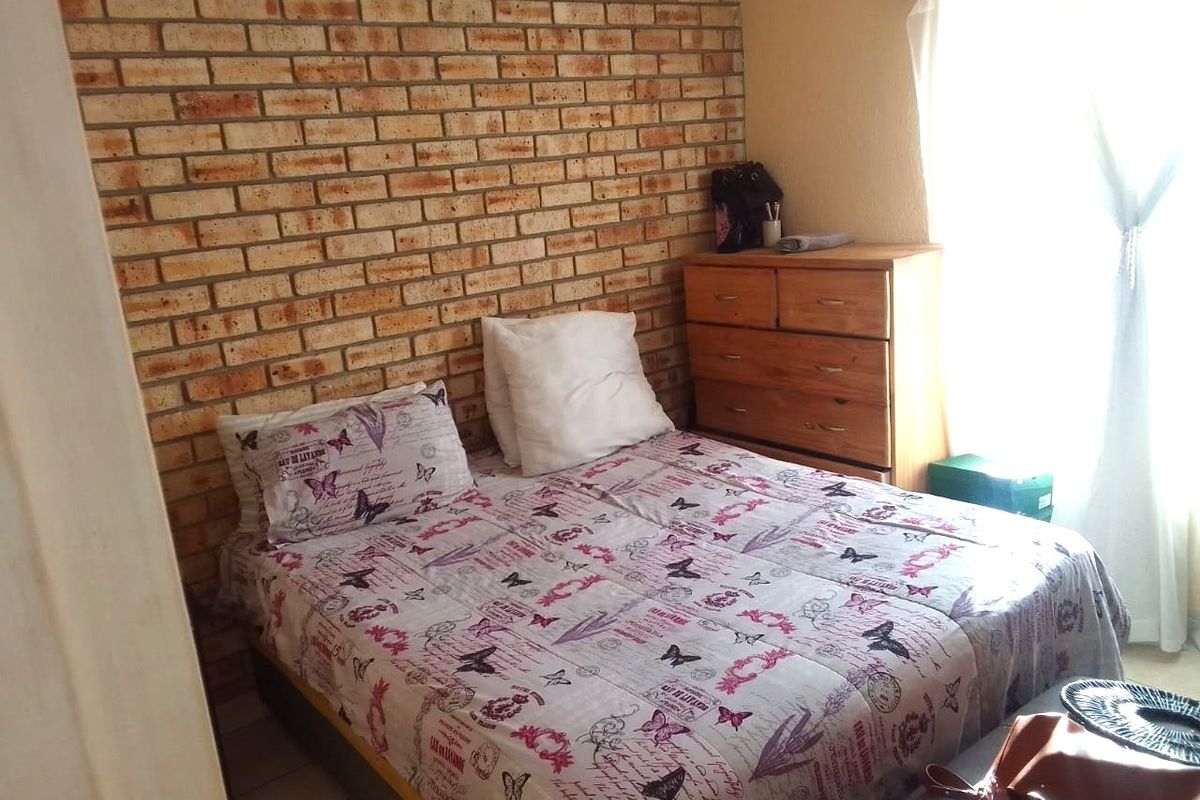 A bedroom featuring an exposed brick feature wall and tiled flooring, offering a rustic aesthetic with natural light from the window.